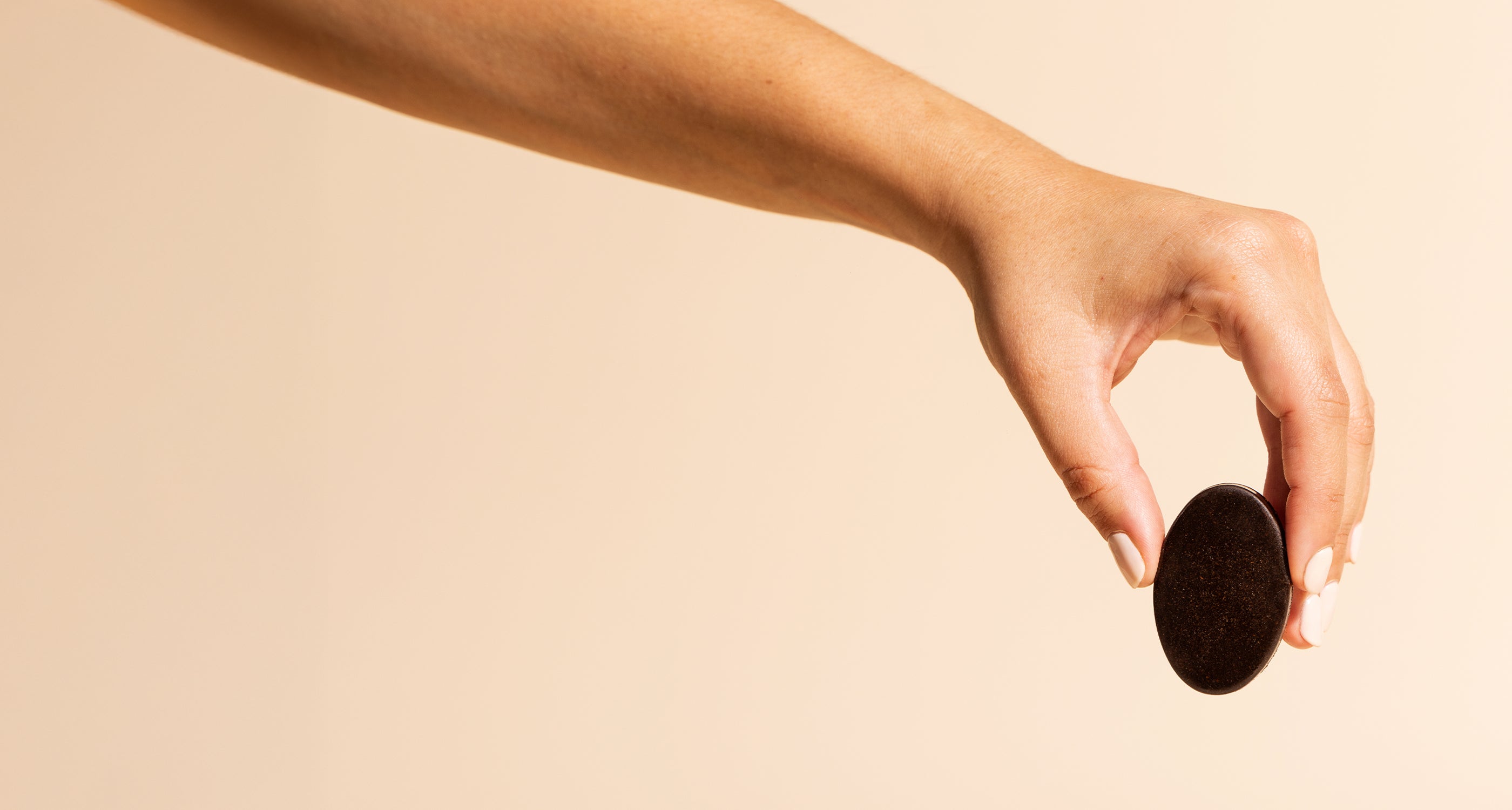 A woman's hand grabbing Compound's chocolate medallion on a beige background
