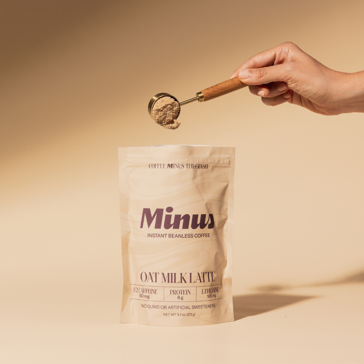 A woman's hand scooping an instant oat milk latte in a pouch named Minus Instant Beanless Coffee