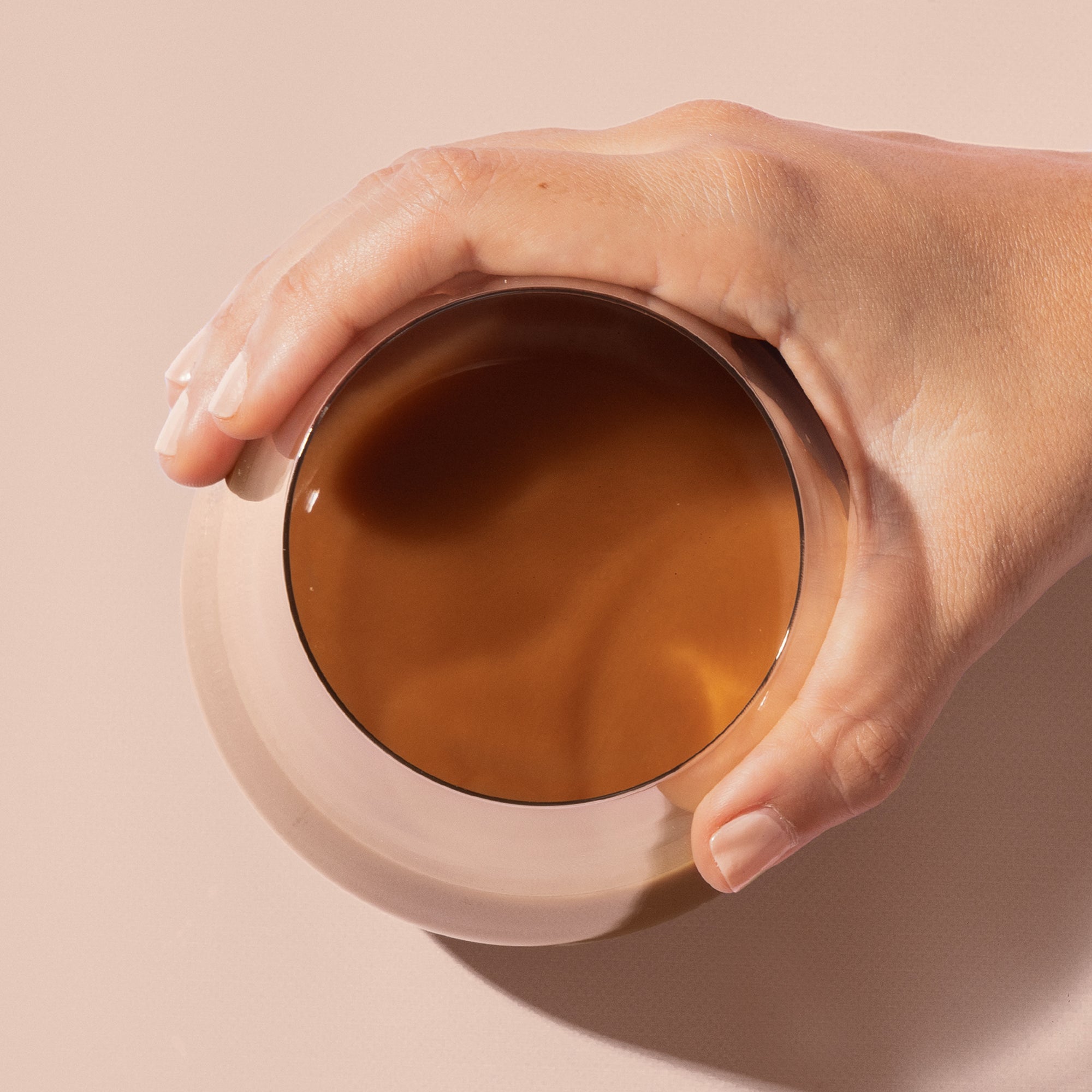Close-up of a woman’s hand holding a latte in a clear glass