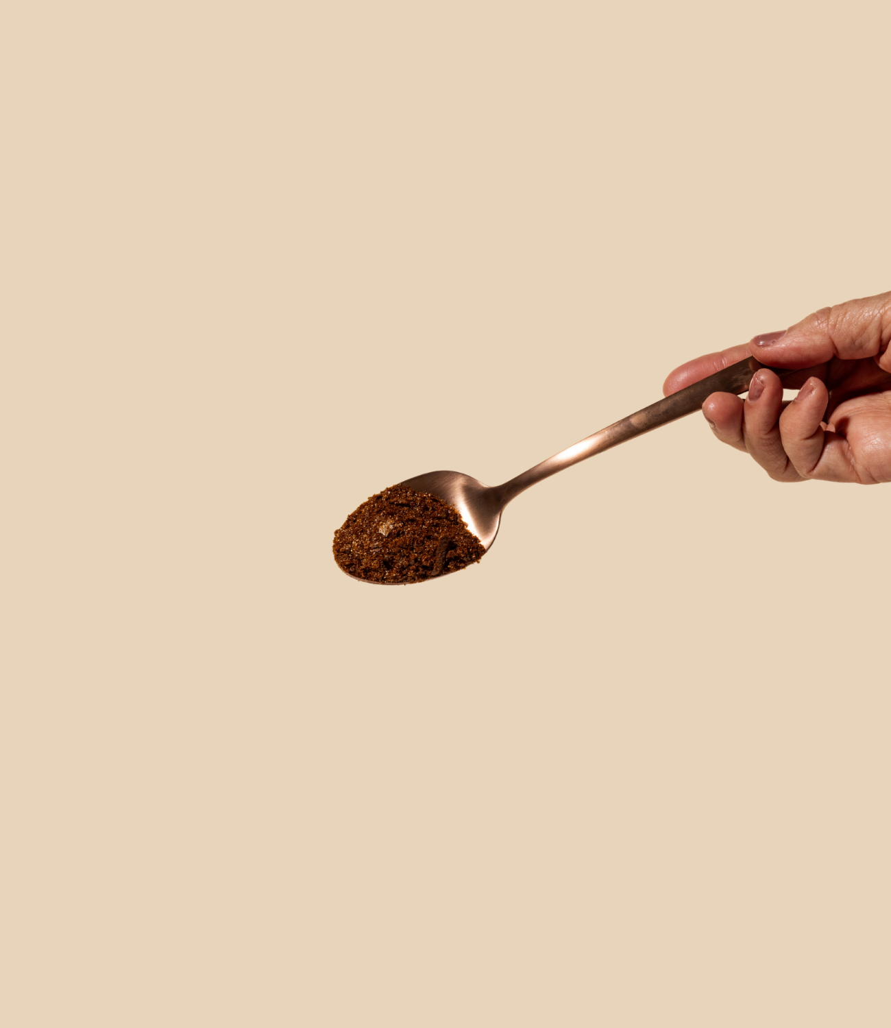 Woman's hand holding a bronze spoon with bean-free instant black coffee