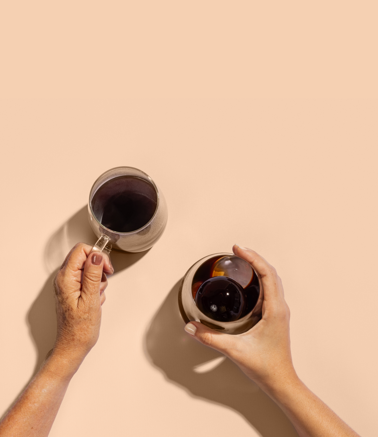 Two women’s hands holding clear glasses of black coffee—one hot, one cold