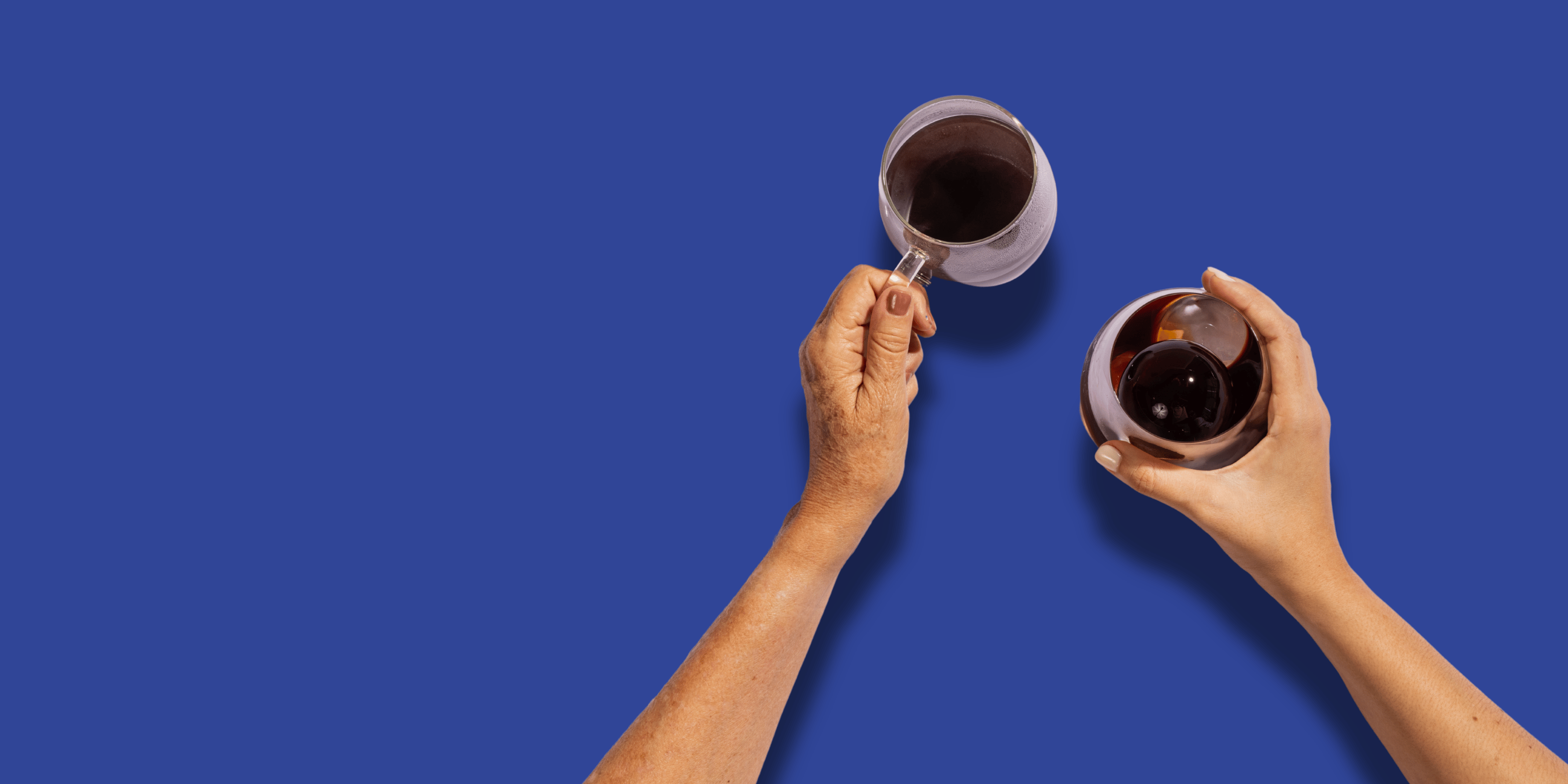 Two hands holding clear cups of coffee. One hot one iced over a blue background