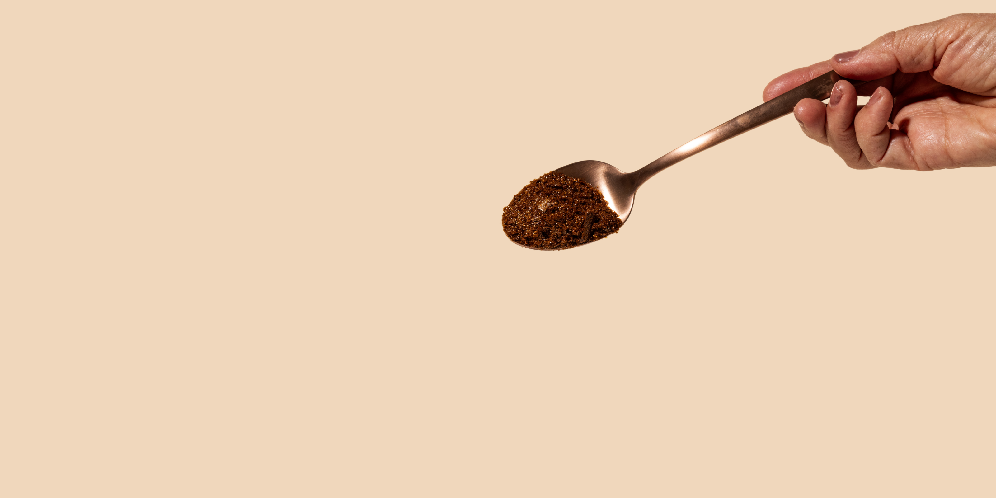 A woman's hand grabbing a bronze spoon with Compound's black instant bean-free coffee