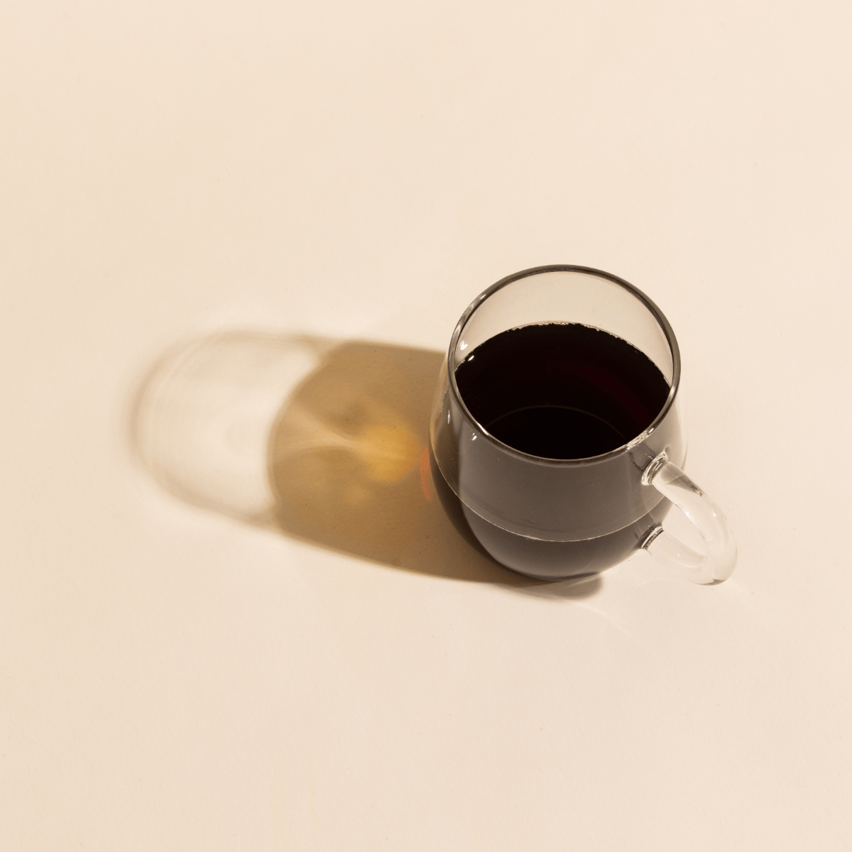 Compound's black instant coffee served in a clear glass over a beige background