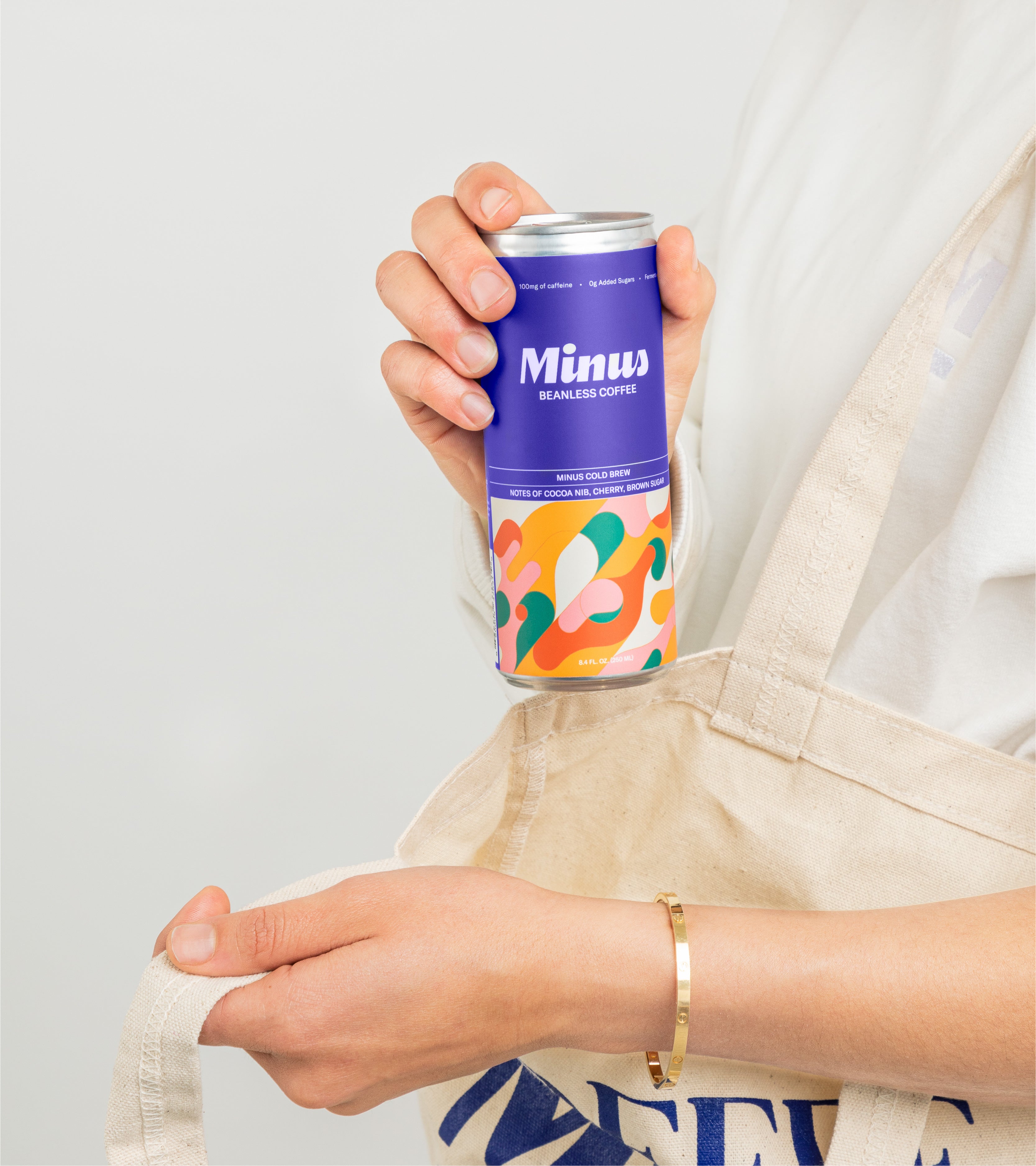 A woman's hand pulling out of a tote bag an RTD beanless cold brew coffee can titled Minus