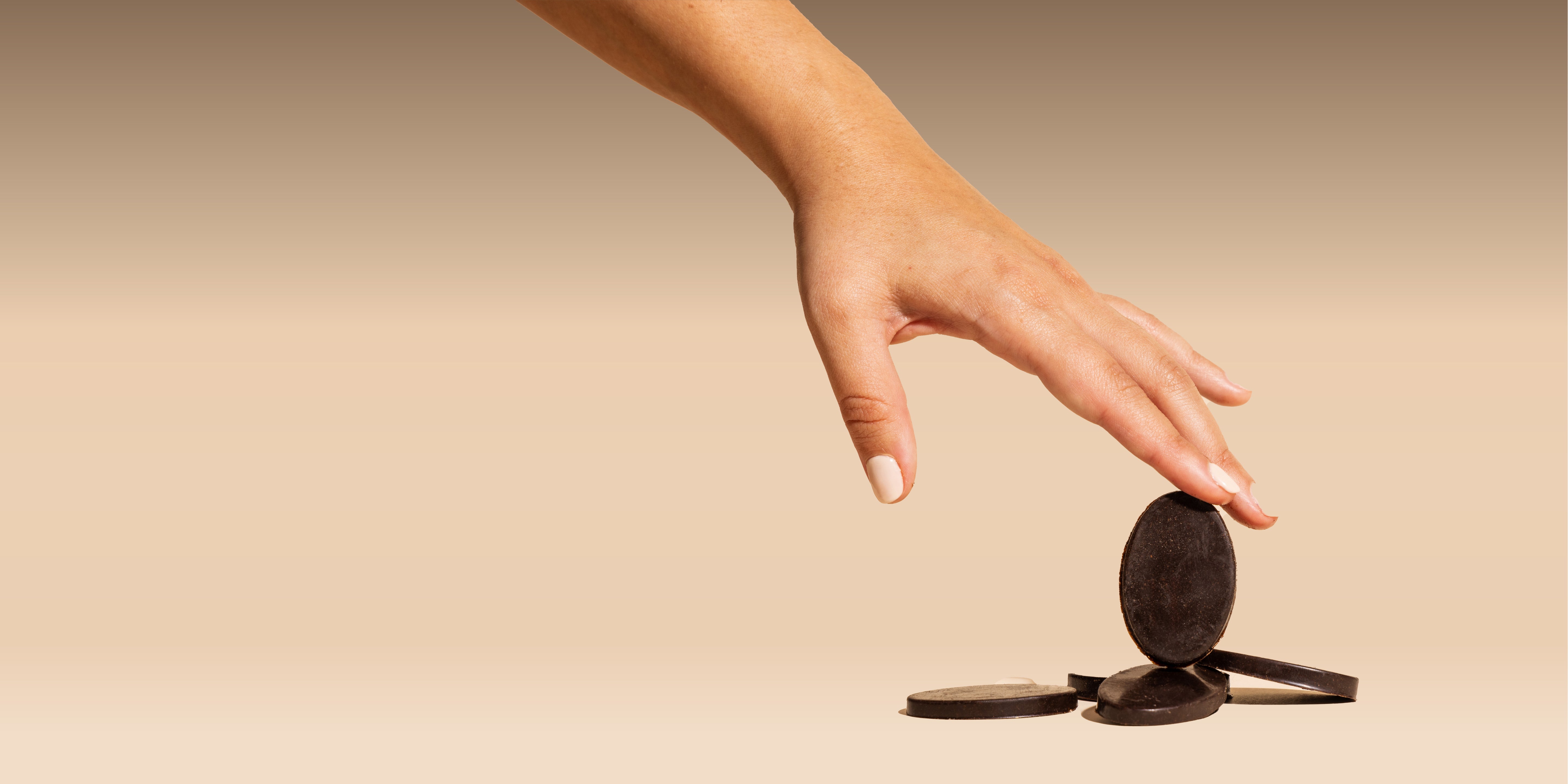 A woman’s hand balancing one of Compound’s cocoa-free chocolate medallions on a stack of others