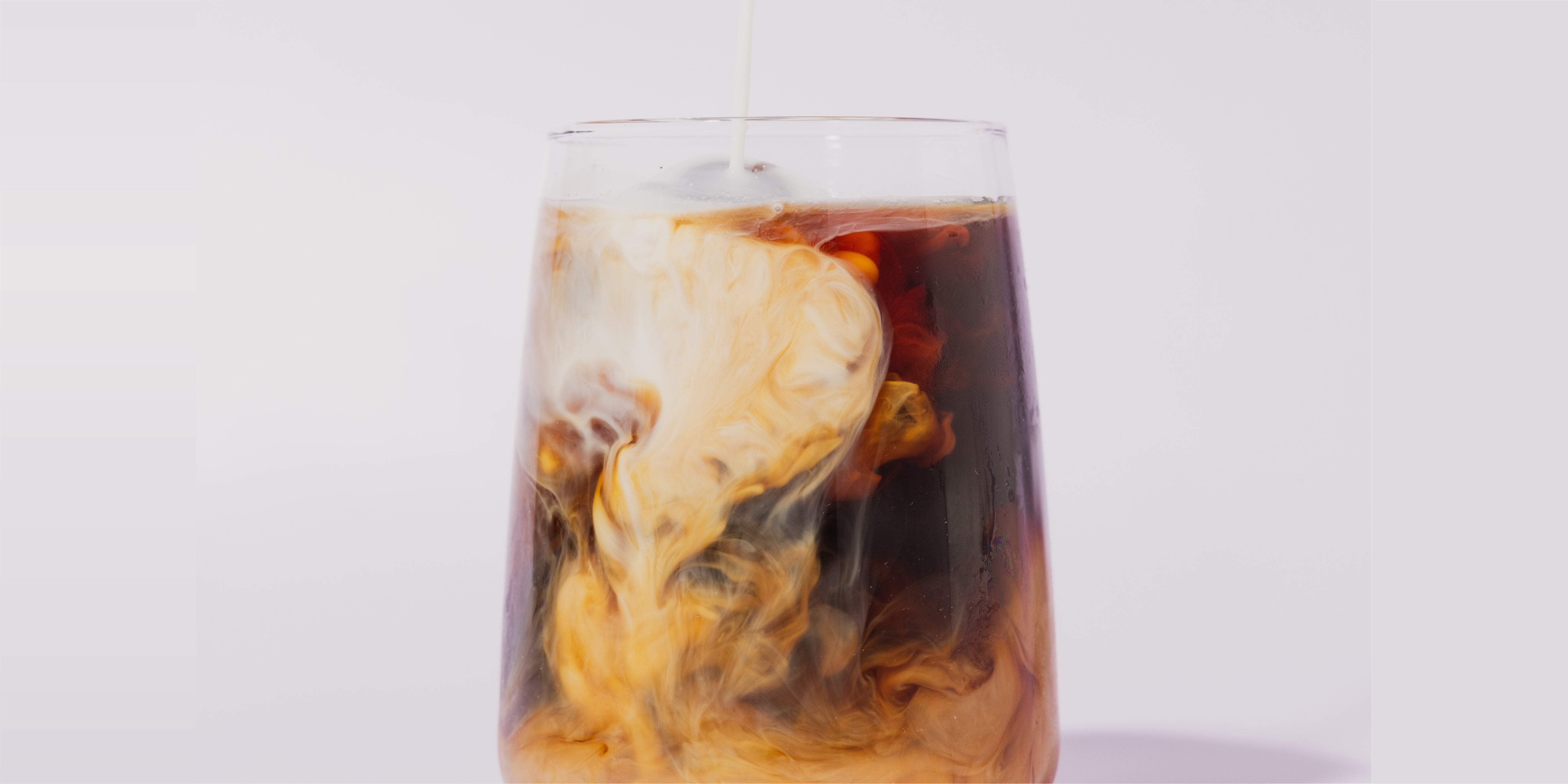 A clear glass of black cold brew coffee with milk being poured in, creating a swirl