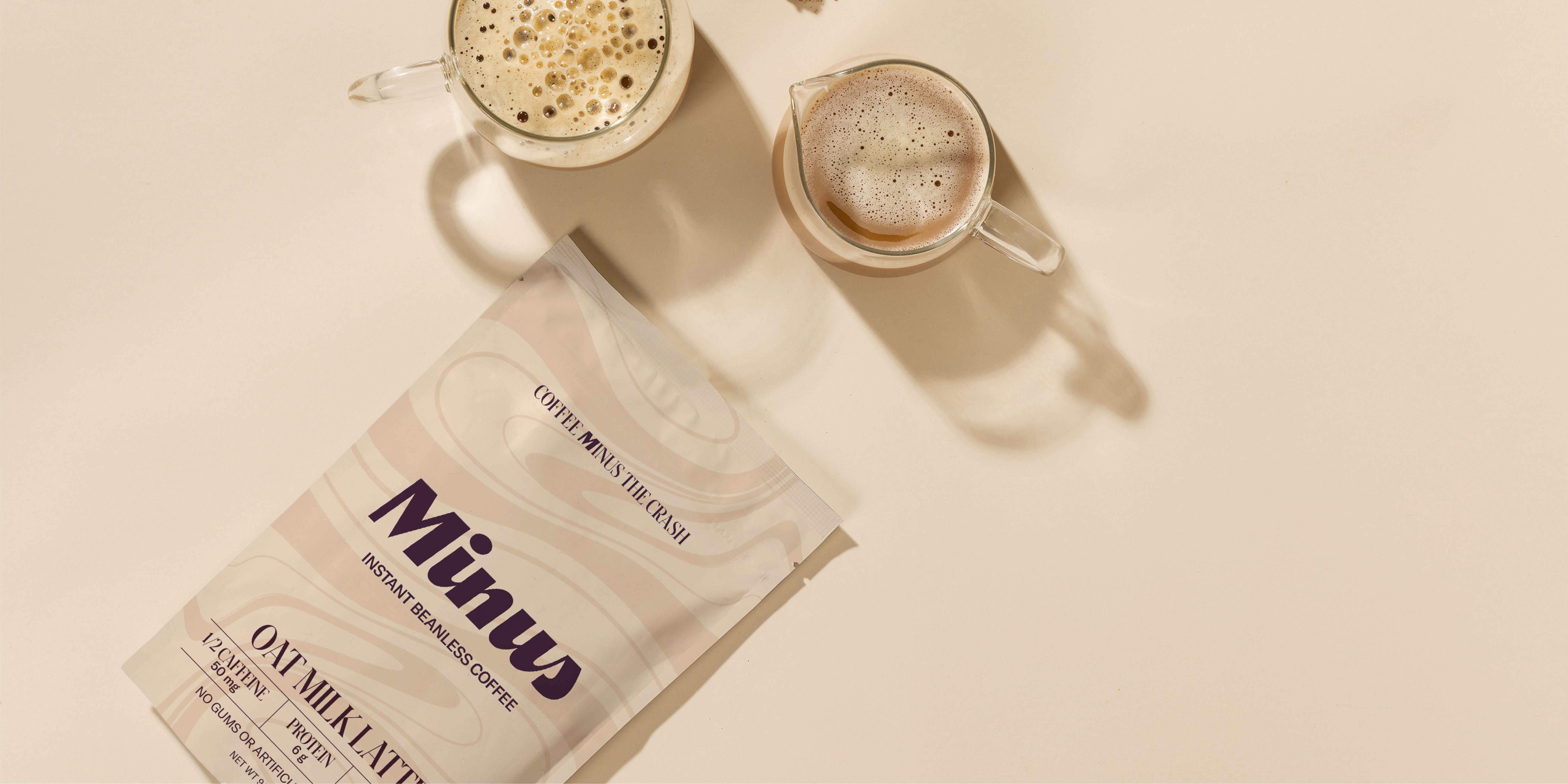 Overhead view of a Minus Instant Beanless Coffee Oat Milk Latte pouch with two prepared lattes in clear glasses