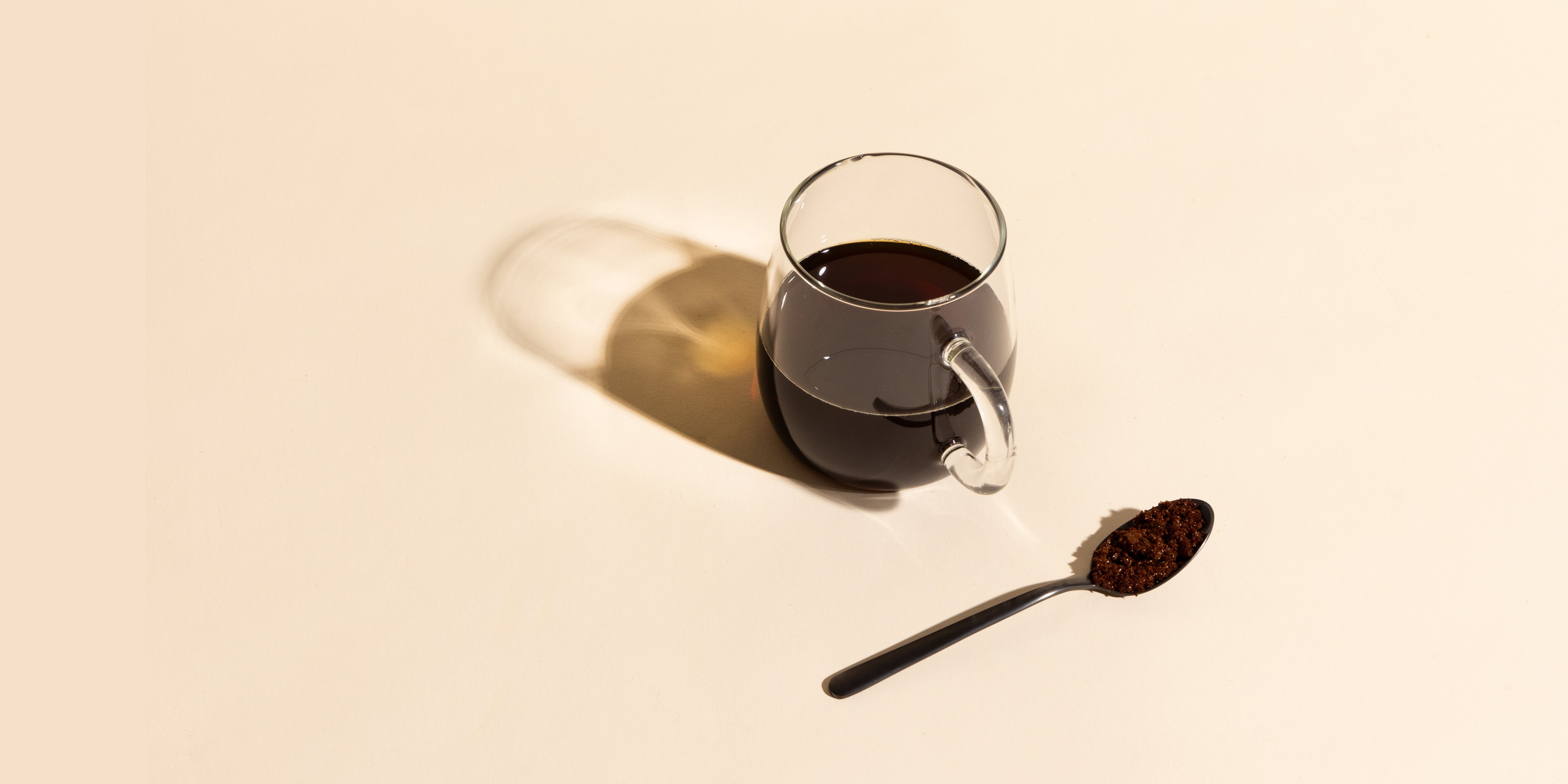 Compound hot coffee served on a clear glass with a black spoon next to it filled with bean-free instant coffee